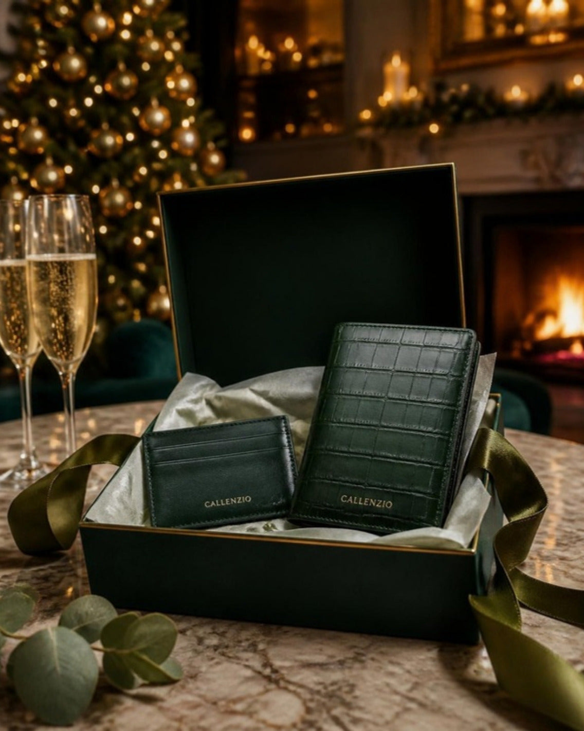 Callenzio Geschenkset in der Geschenkbox vor Kaminfeuer und Weihnachtsbaum, daneben zwei Sektgläser